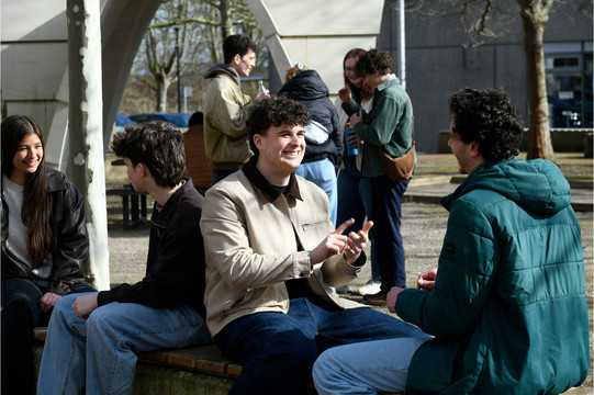 Studierende sitzen draußen am Campus Süd und unterhalten sich.