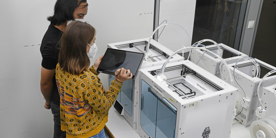 Students stand in front of 3D printers and assess progress.