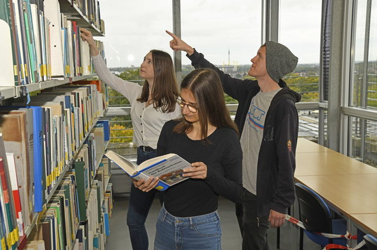 Studenten stehen vor Bücherregal.