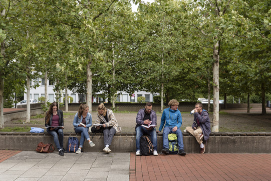 Studierende sitzen auf einer langen Bank auf dem Campus Süd und schauen in Bücher.