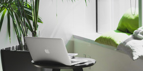 Arbeitsplatz Ein kleiner gemütlicher Arbeitsbereich mit Sitzgelegenheit, Pflanzen und einem Tisch, auf dem ein Laptop platziert ist.