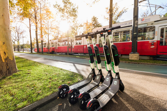 Öffentliche Verkehrsmittel (Modul 21) Im Hintergrund fährt eine Straßenbahn und im Vordergrund sind E-Scooter platziert.