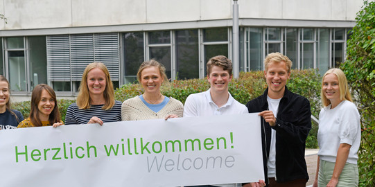 Titelbild Erstis Studierende stehen mit einem Herzlich Willkommen-Banner vor dem GB3.