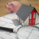 Wohnungsmarkt (Modul 24) Ein Modellhaus steht auf einem Bauplan mit einer Lupe und einem Sparschwein daneben.