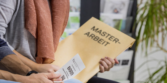 Abgabe Masterarbeit Mensch mit Master-Arbeit-Umschlag sitzt im Warteraum.