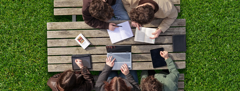 Studierende werden von der Vogelperspektive beim arbeiten draußen an einem Tisch gezeigt.