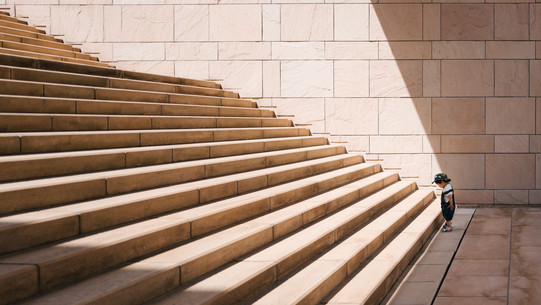 Kleines Kind steht vor langer Treppe mit großen Stufen.