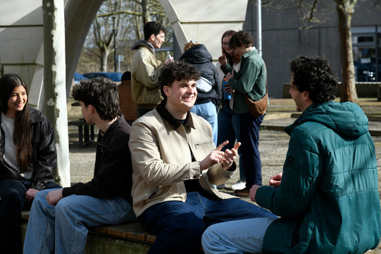 Studierende sitzen draußen am Campus Süd und unterhalten sich.